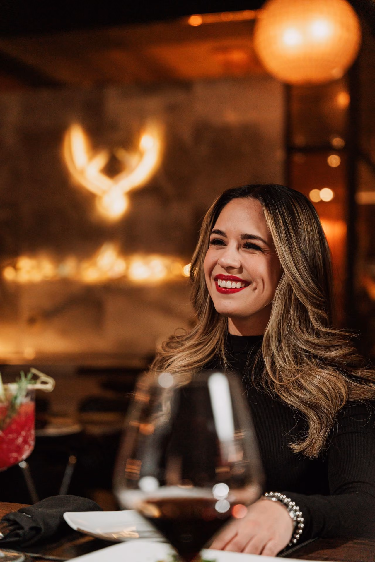 Invitada sonriendo con copa de vino y el logo iluminado al fondo