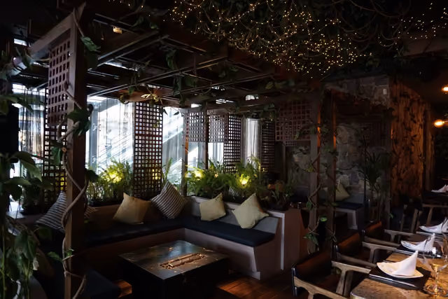 Salón lounge de Mochomos Metepec con sillones, celosías de madera y luces entre las plantas