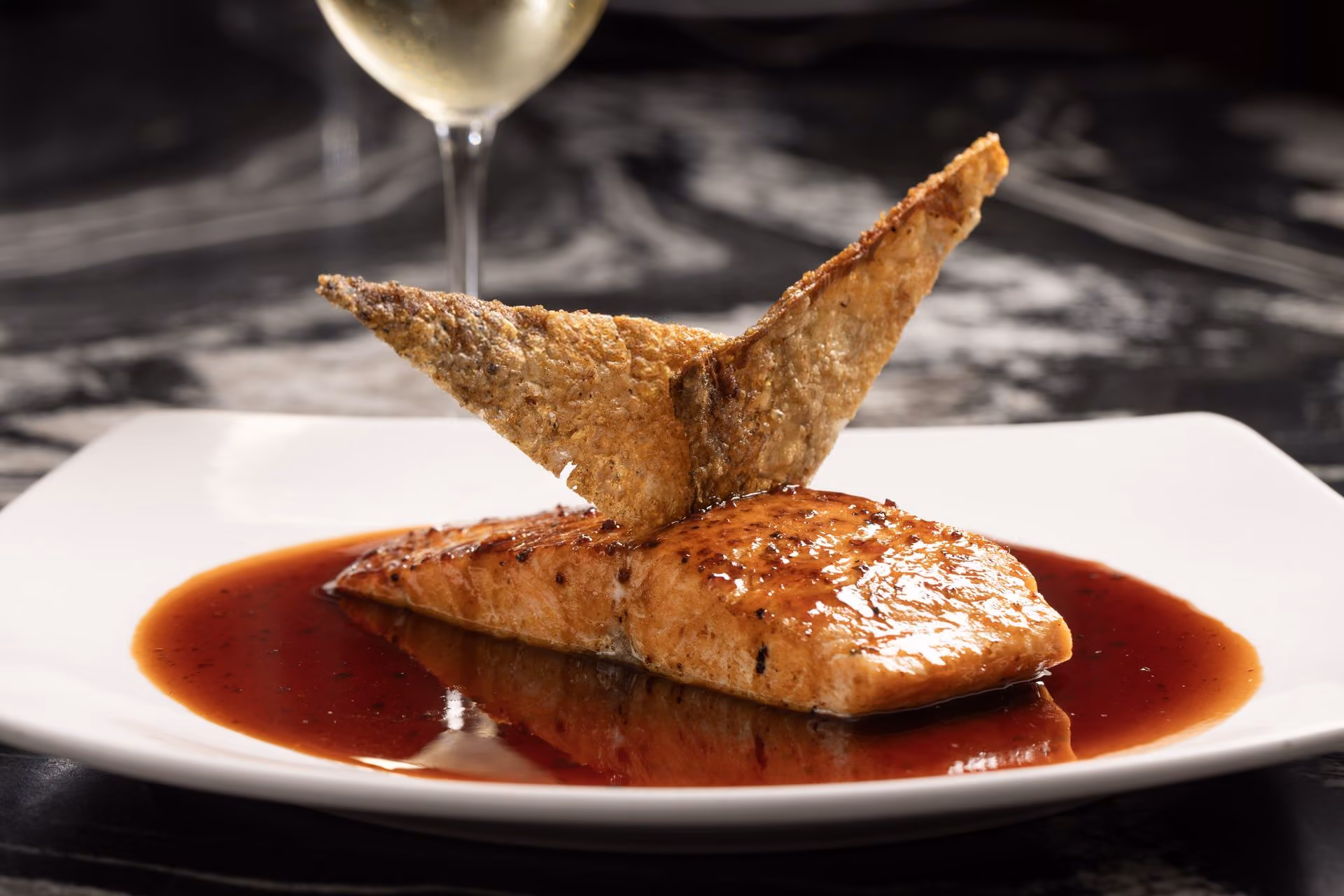 Salmón glaseado con crujiente encima y copa de vino blanco
