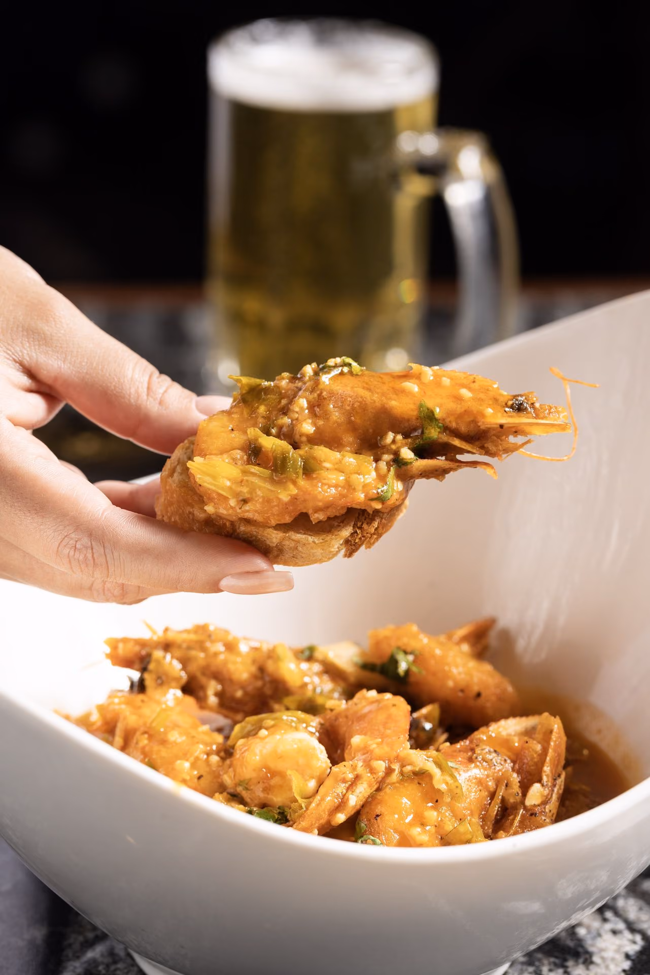 Camarón tomado del plato, con cerveza al fondo