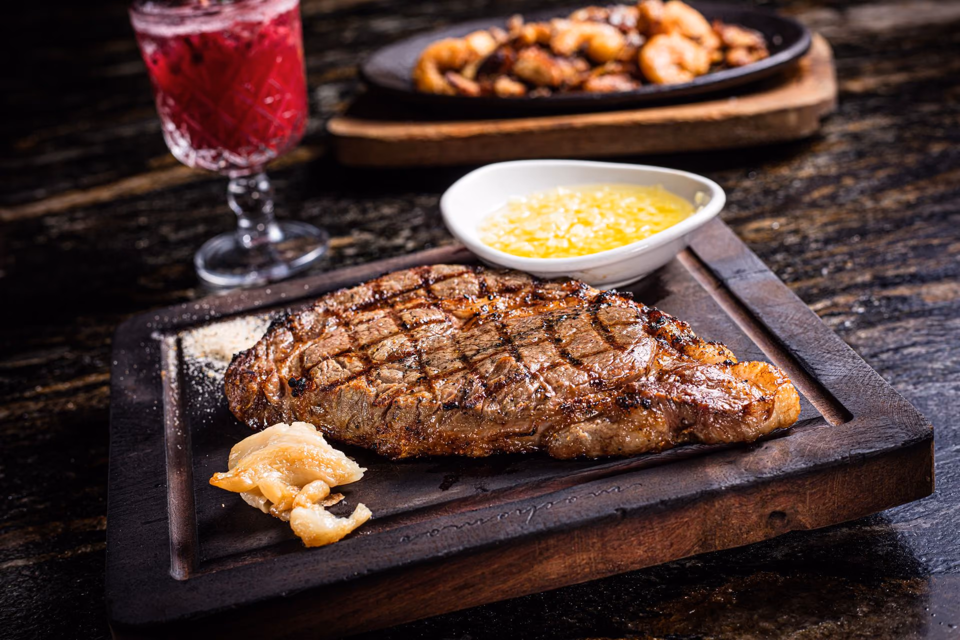 Corte a la parrilla en tabla con mantequilla y camarones al fondo