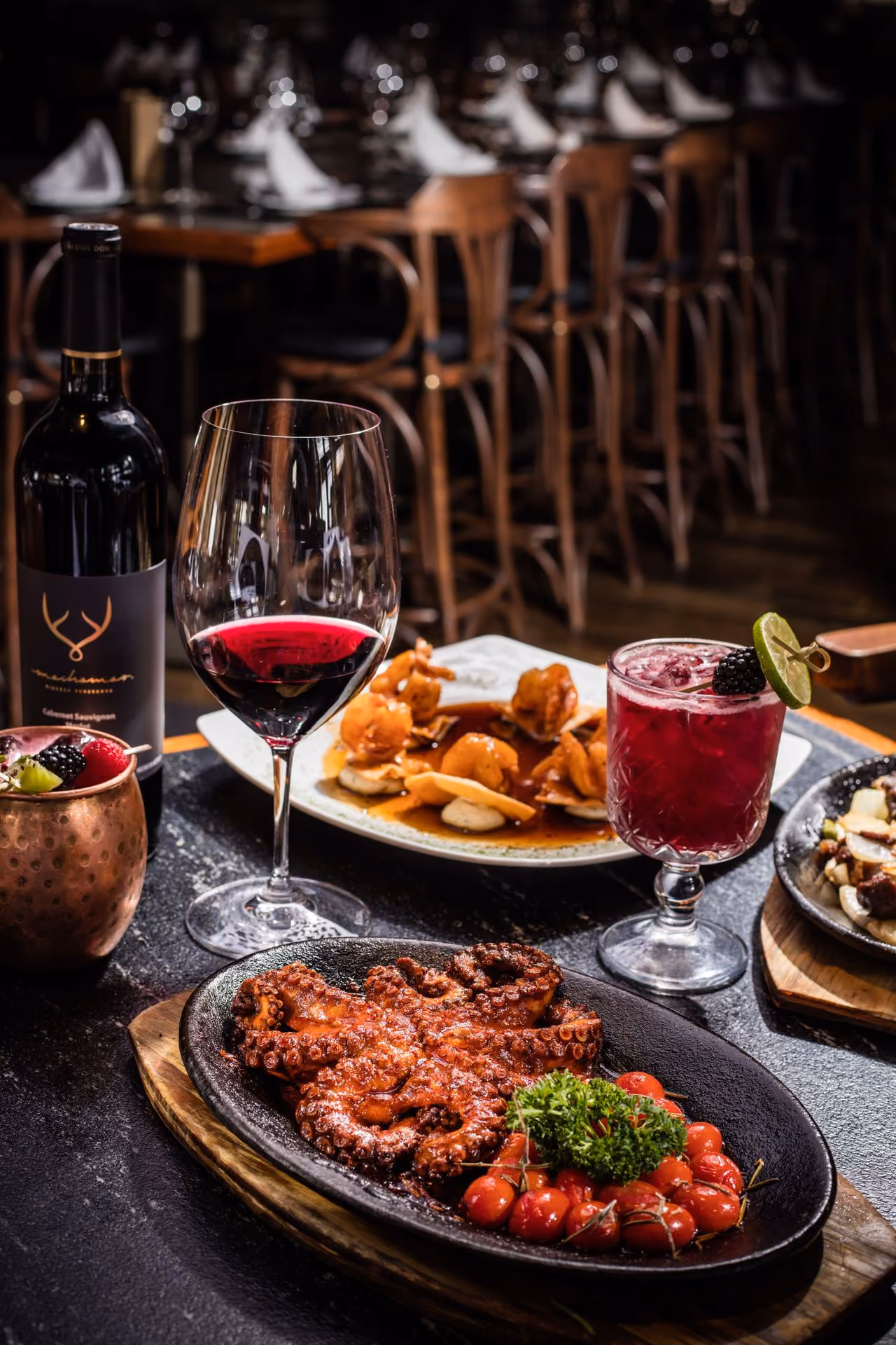 Pulpo en plato de hierro con tomates y copas de vino