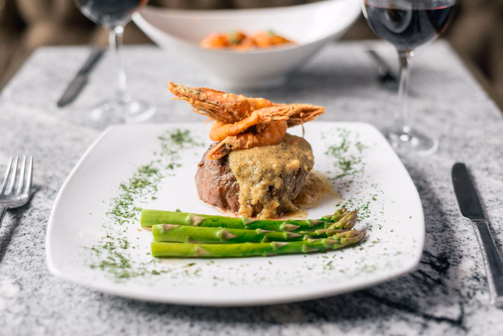 Filete con camarón crujiente y espárragos en plato blanco