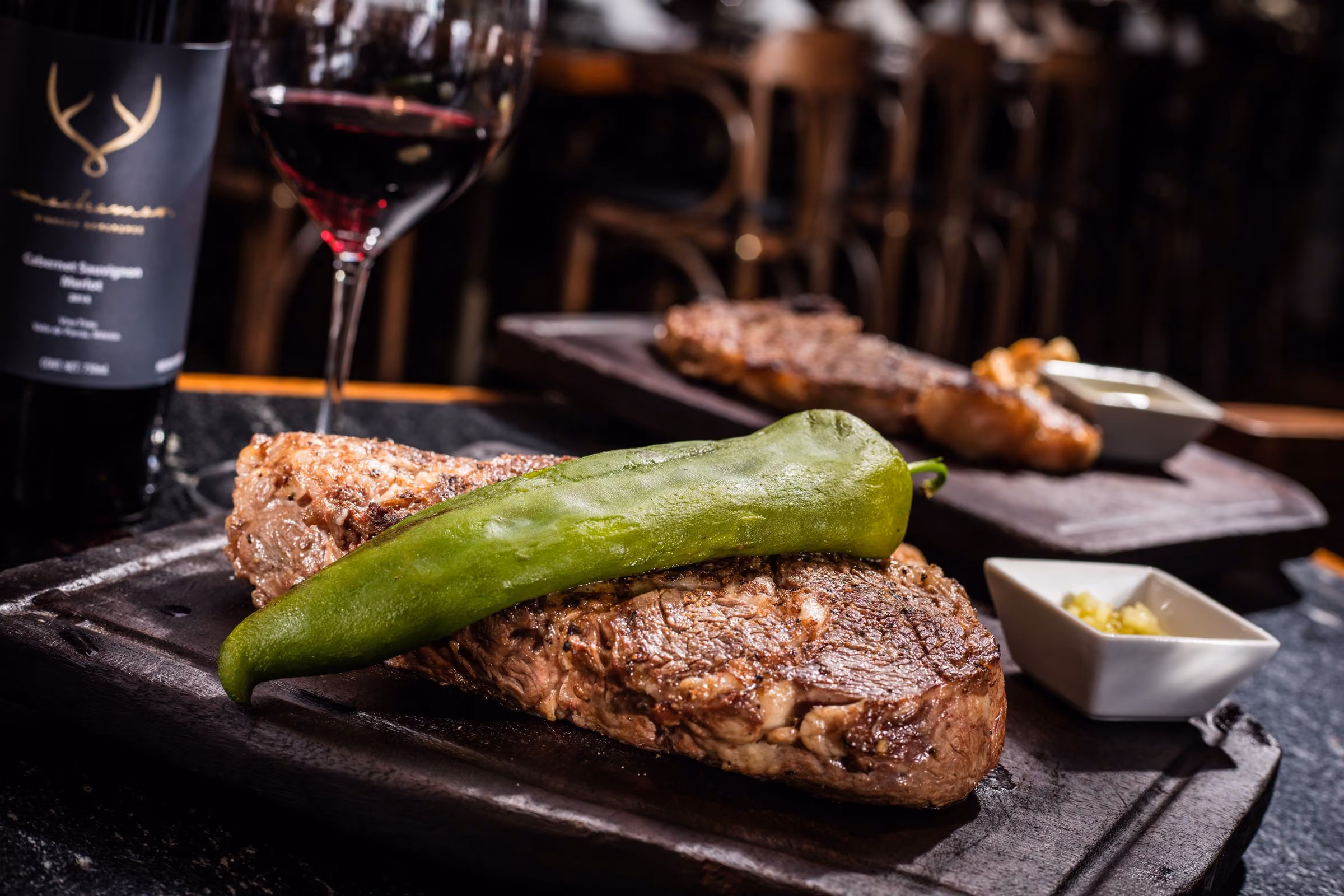 Corte con chile güero asado en tabla, con copa y botella de vino de la casa