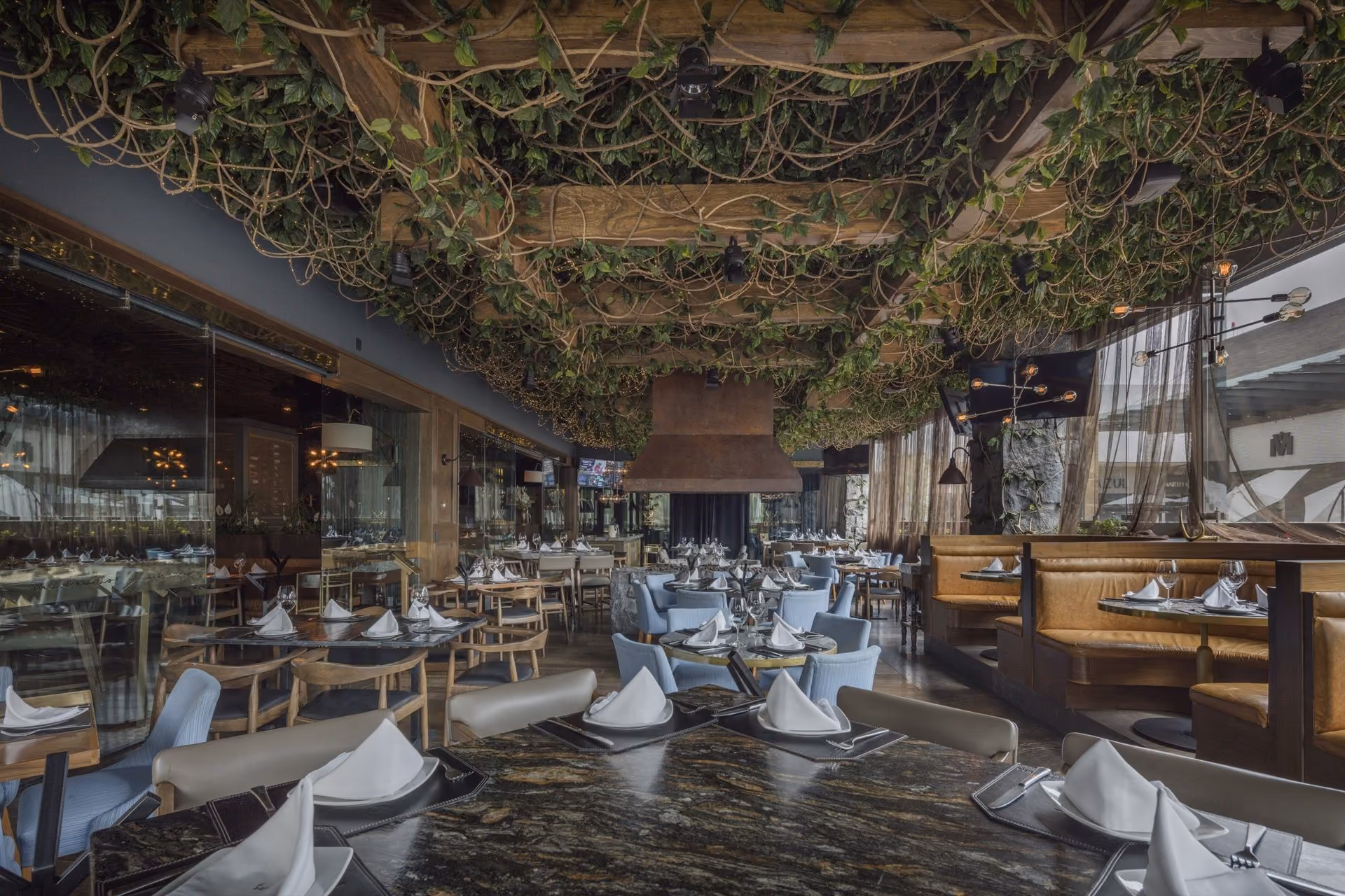 Salón de Mochomos Puebla bajo el techo de enredadera, con sillas azules y gabinetes de piel